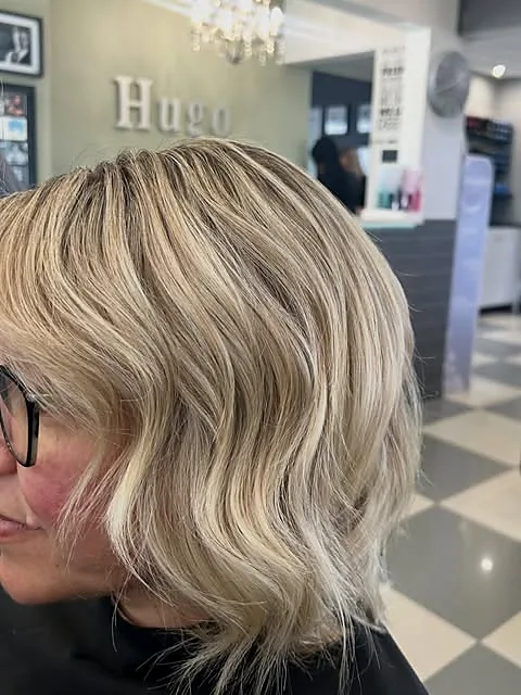 A blended blonde bob, photographed in the salon with the Hugo sign behind